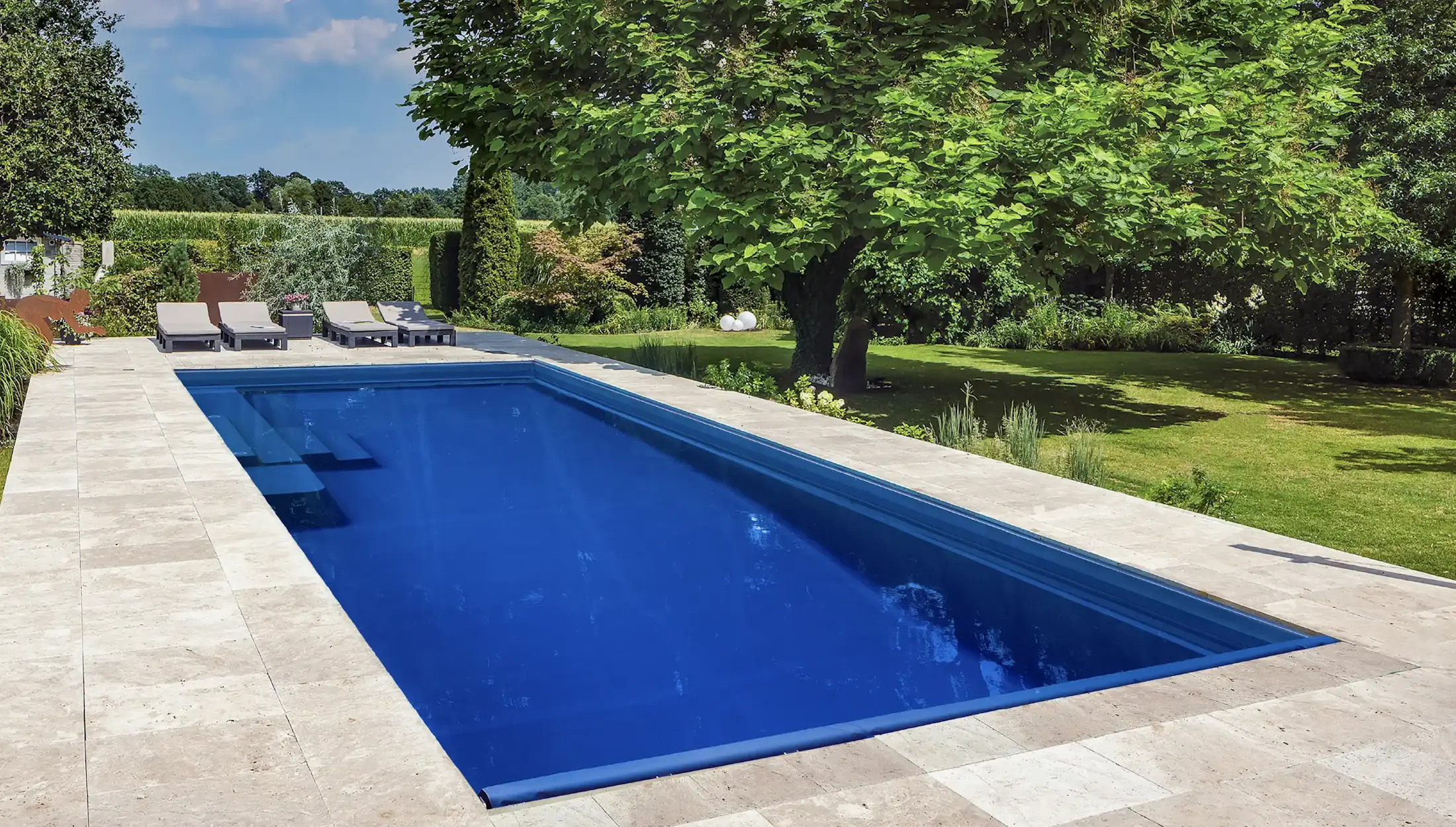 Rectangular pool with travertine deck surrounded by lush garden